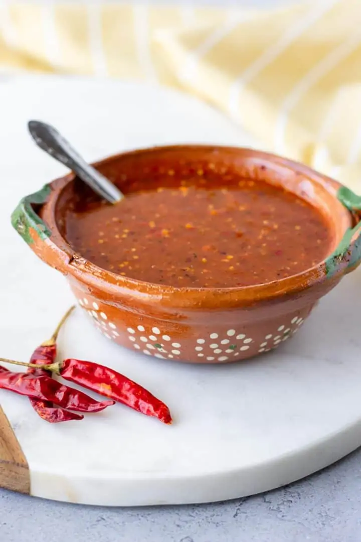 Salsa in a clay bowl with chile de arbol pods on the plate.