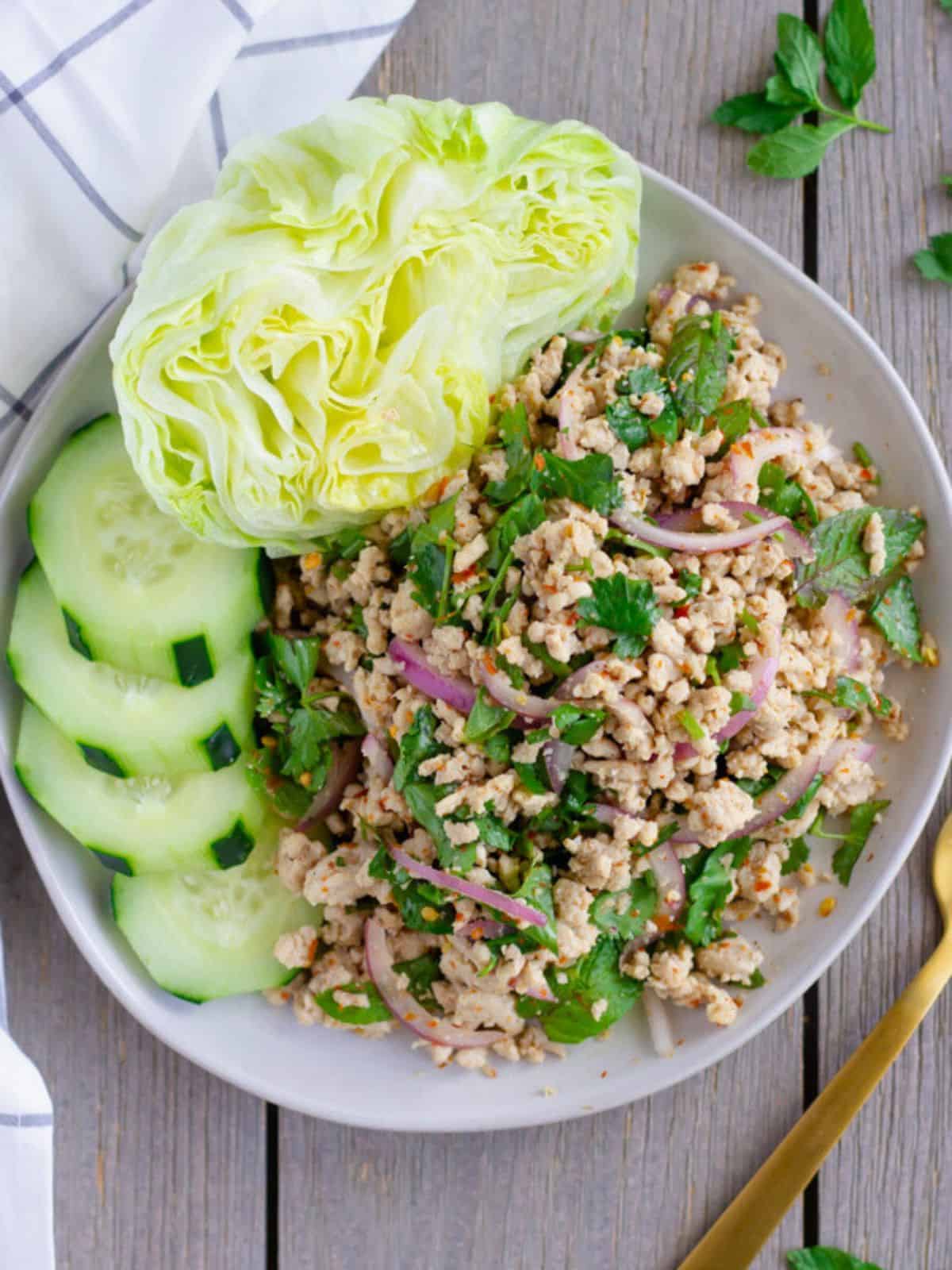 Overhead view of laab gai on a plate with cucumbers and lettuce.