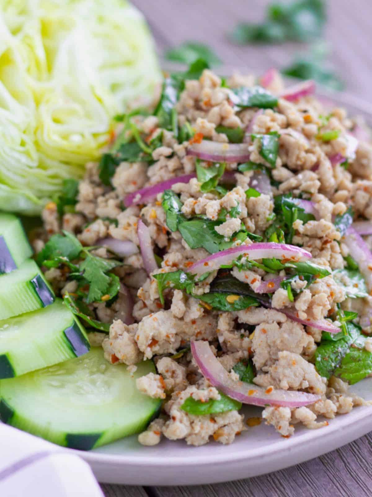 Thai ground chicken salad on a plate with cucumbers and lettuce.